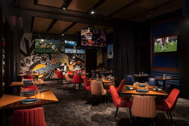Modern sports-themed restaurant with colorful seating, wall art, and multiple TVs showing different games.