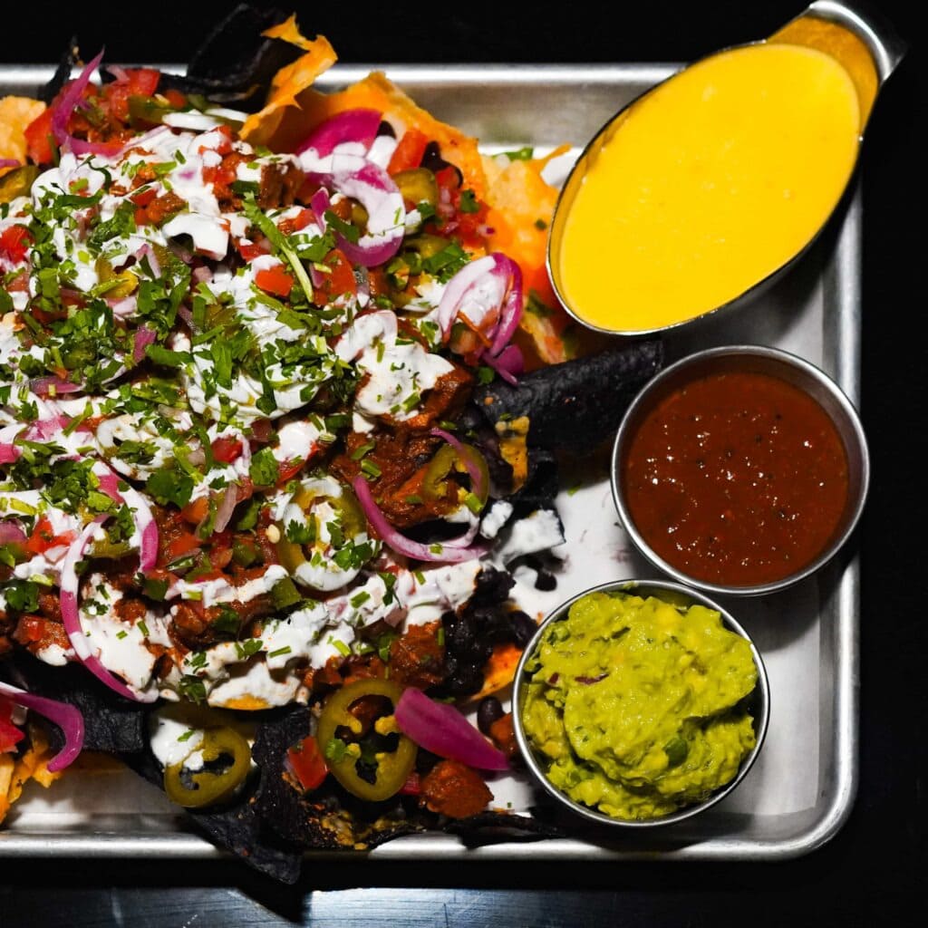 Loaded nachos with jalapeños, onions, cilantro, and sauces on a tray with cheese, salsa, and guacamole.