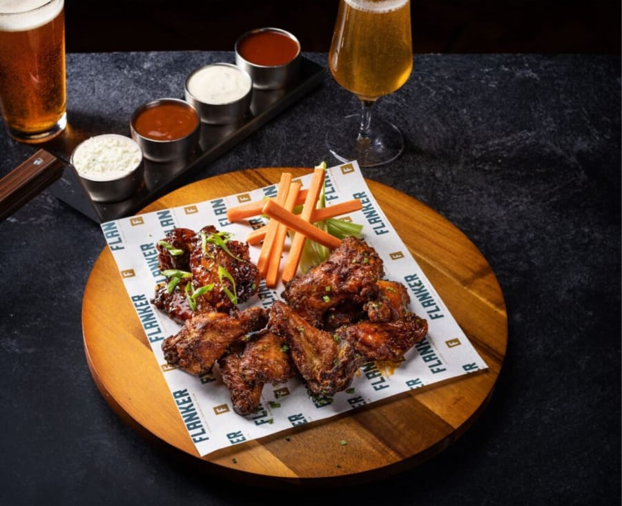 Plate of chicken wings served with celery, carrot sticks, and dipping sauces, with glasses of beer on the table