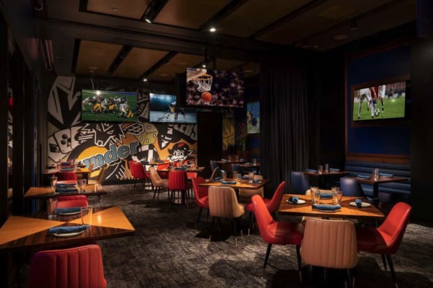 Modern sports bar interior with dining tables, colorful chairs, and multiple TVs showing live games