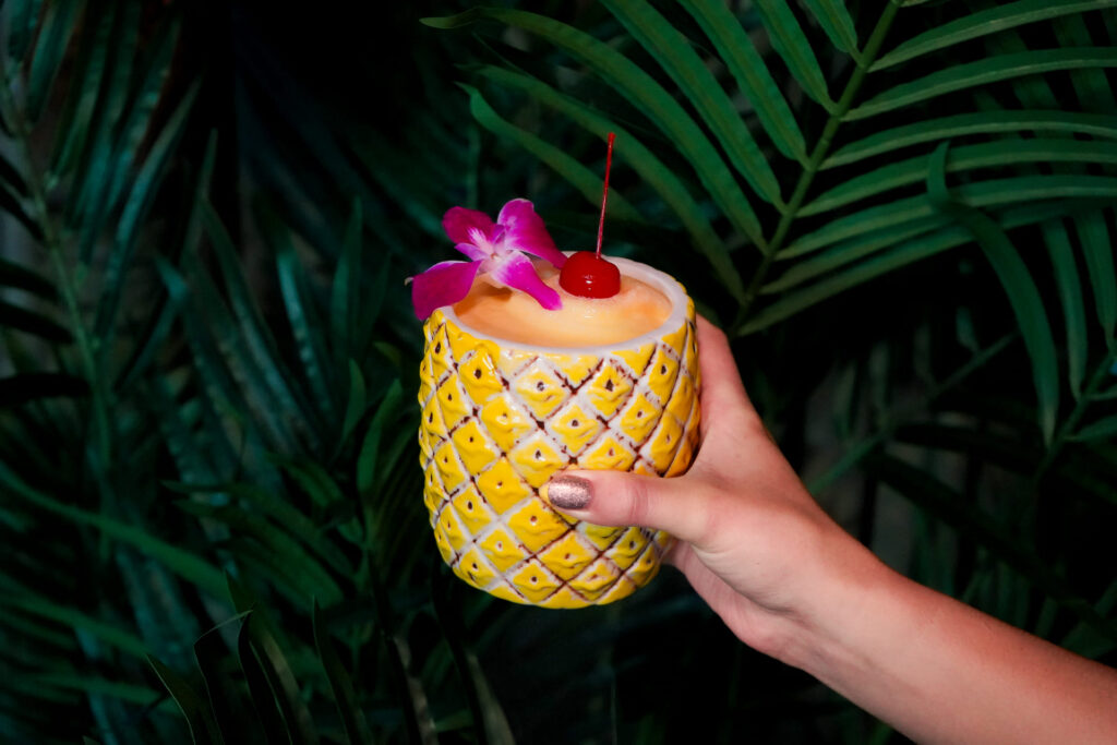 Image pop-up Frozen tropical cocktail served in a pineapple-shaped mug with a cherry and orchid garnish.