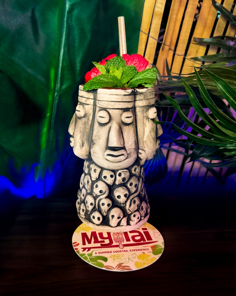 Image pop-up Signature My Tai cocktail served in a decorative tiki vessel with mint and watermelon garnish.