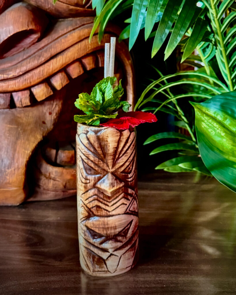Image pop-up Tropical cocktail served in a carved tiki mug with fresh mint and fruit garnish.