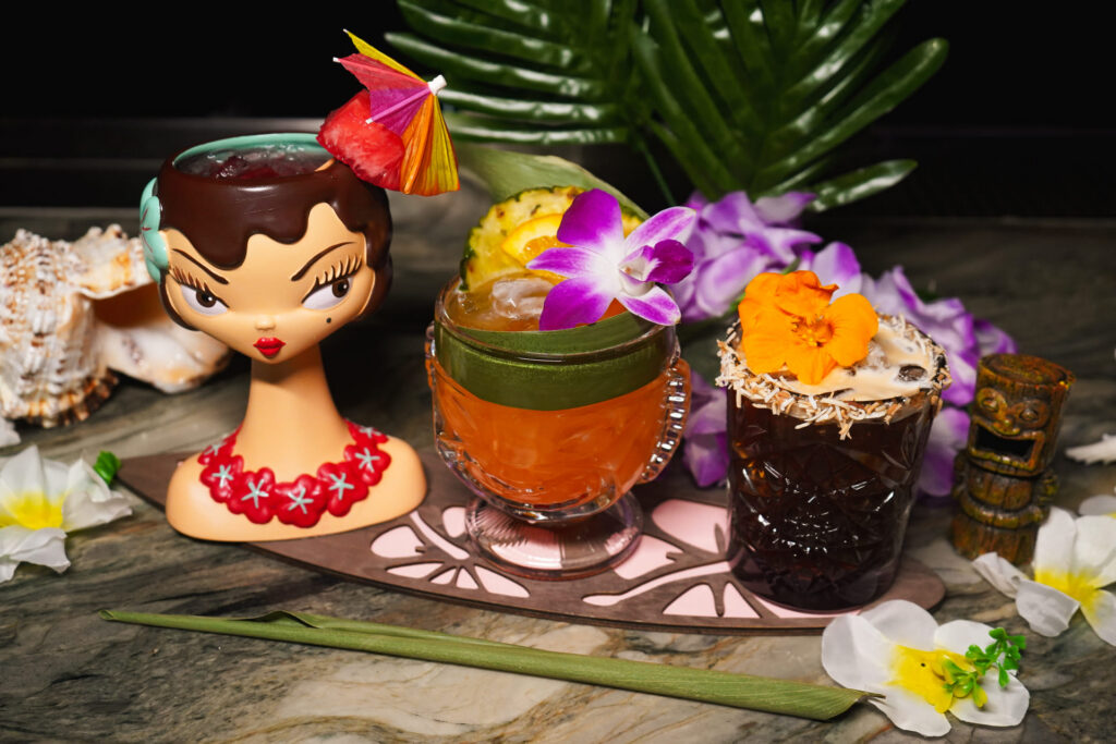 Image pop-up Assortment of tropical cocktails served in decorative tiki-inspired glassware with fruit and floral garnishes.