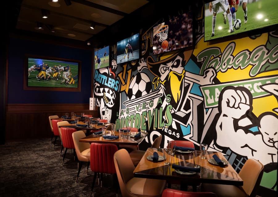 Flanker dining area with colorful Las Vegas sports murals, table seating, and multiple screens showing live sports.