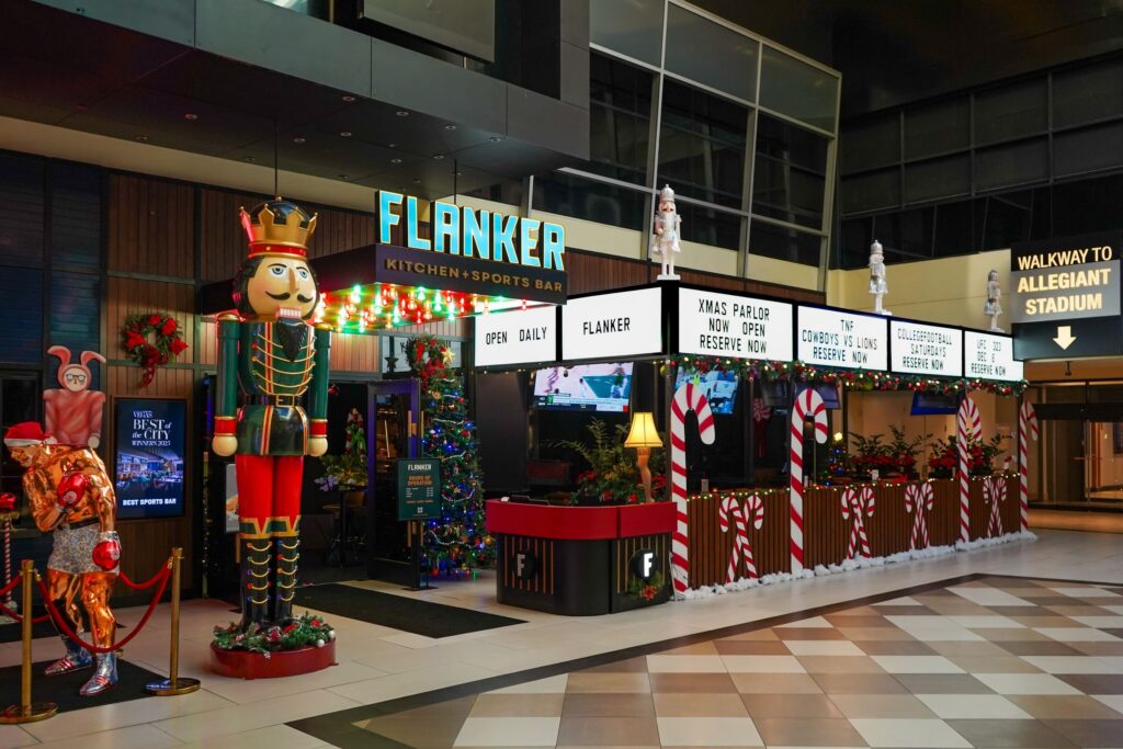 Image pop-up Flanker Kitchen + Sports Bar entrance decorated with a giant nutcracker, Christmas trees, colorful lights, candy canes, and holiday-themed signage.