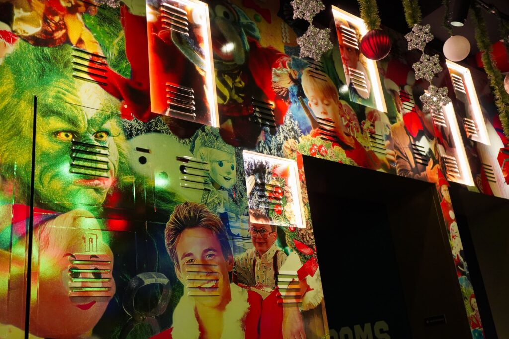 Image pop-up Colorful Christmas movie mural featuring the Grinch and other holiday characters, illuminated wall panels, hanging snowflakes, and red Christmas ornaments.